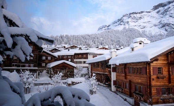group of wooden condos covered in thick snow, surrounded by snow-covered forest and mountains