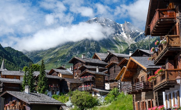 group of wooden condos nestled in the mountainside, with small bit of snow on the mountain peaks as they cut through the clouds